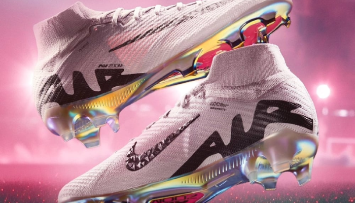 chuteira Nike Mercurial Superfly 9 Elite FG em uma variação de cinza Atmosphere e preto. A chuteira possui detalhes em rosa e iridescente na placa da sola e um Swoosh da Nike com estampa geométrica. O texto descritivo menciona que a chuteira é leve, confortável e oferece ótimo toque de bola, ideal para jogadores rápidos que buscam desempenho e estilo em campo.